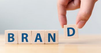 Hand putting wood cube block with word “BRAND” on wooden table.