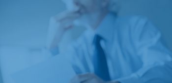 Pensive businessman with hand on chin looking away and holding a document, selective focus, glasses on foreground
